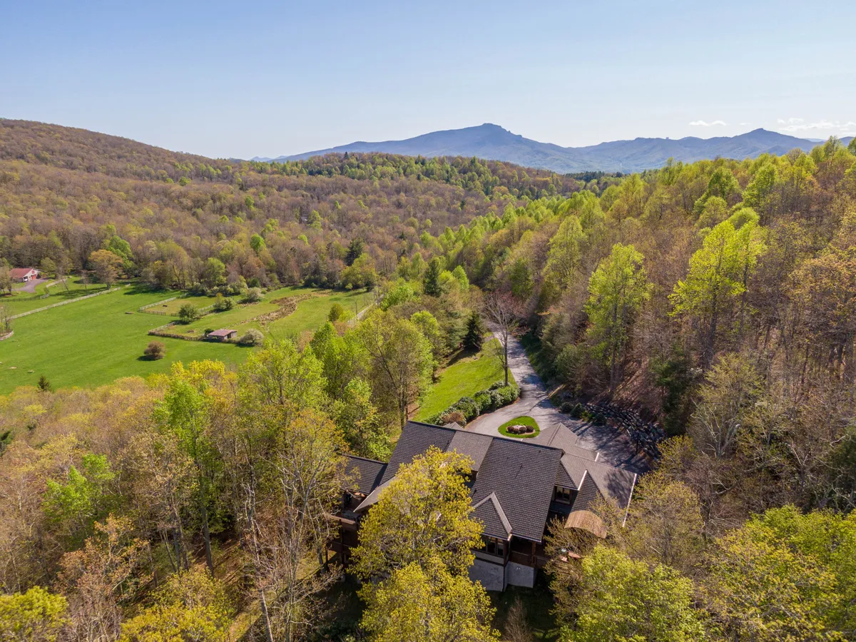 This exterior image showcases Horizon’s Edge nestled among dense trees with a stunning mountain backdrop and a winding driveway leading up to the spacious house. The surrounding natural landscape highlights the property's proximity to outdoor adventure opportunities and mountain trails.