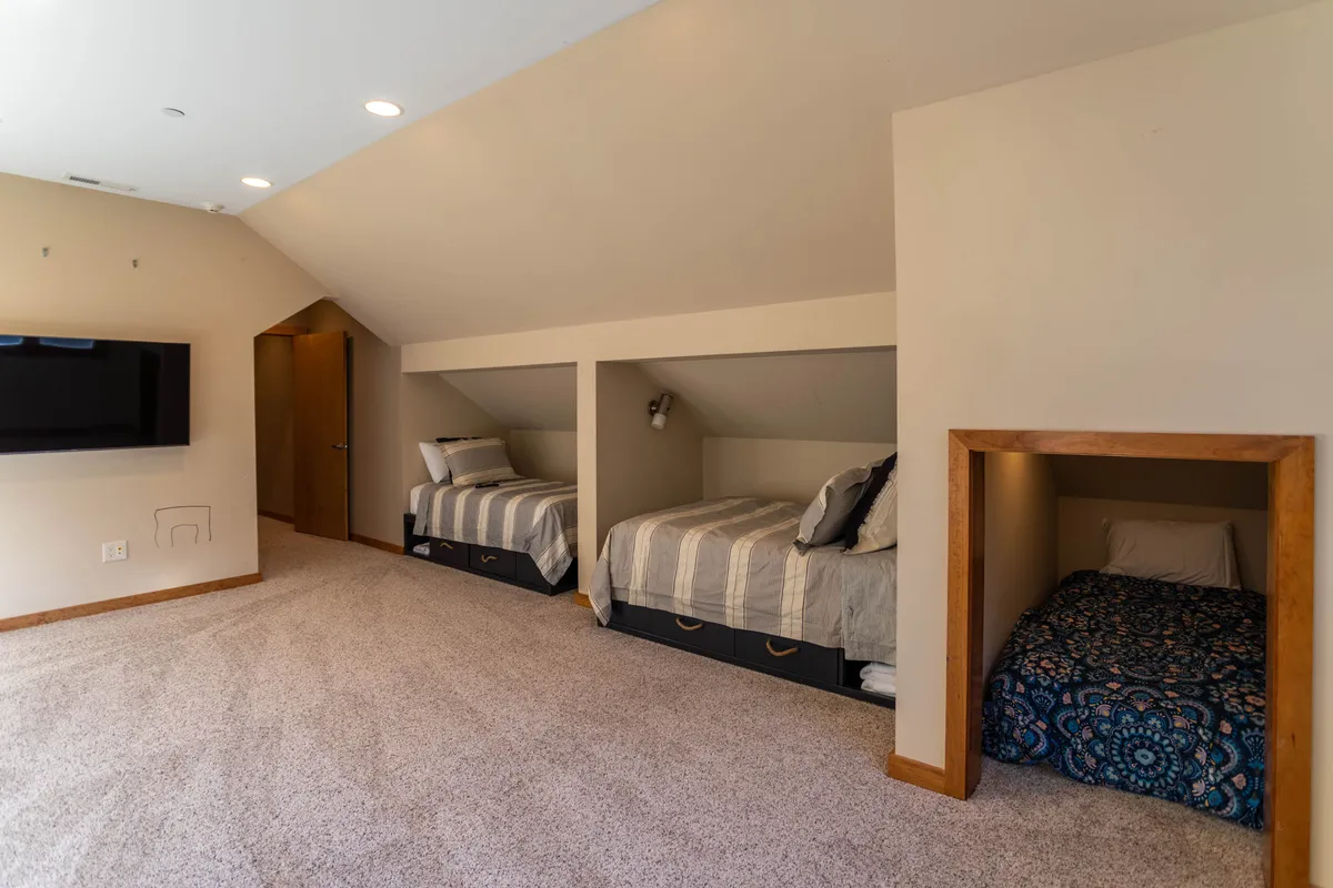 A cozy bunk room with built-in bunk beds, decorative bedding, and a wall-mounted TV. The intimate space is designed for comfort and togetherness, making it ideal for children or groups.