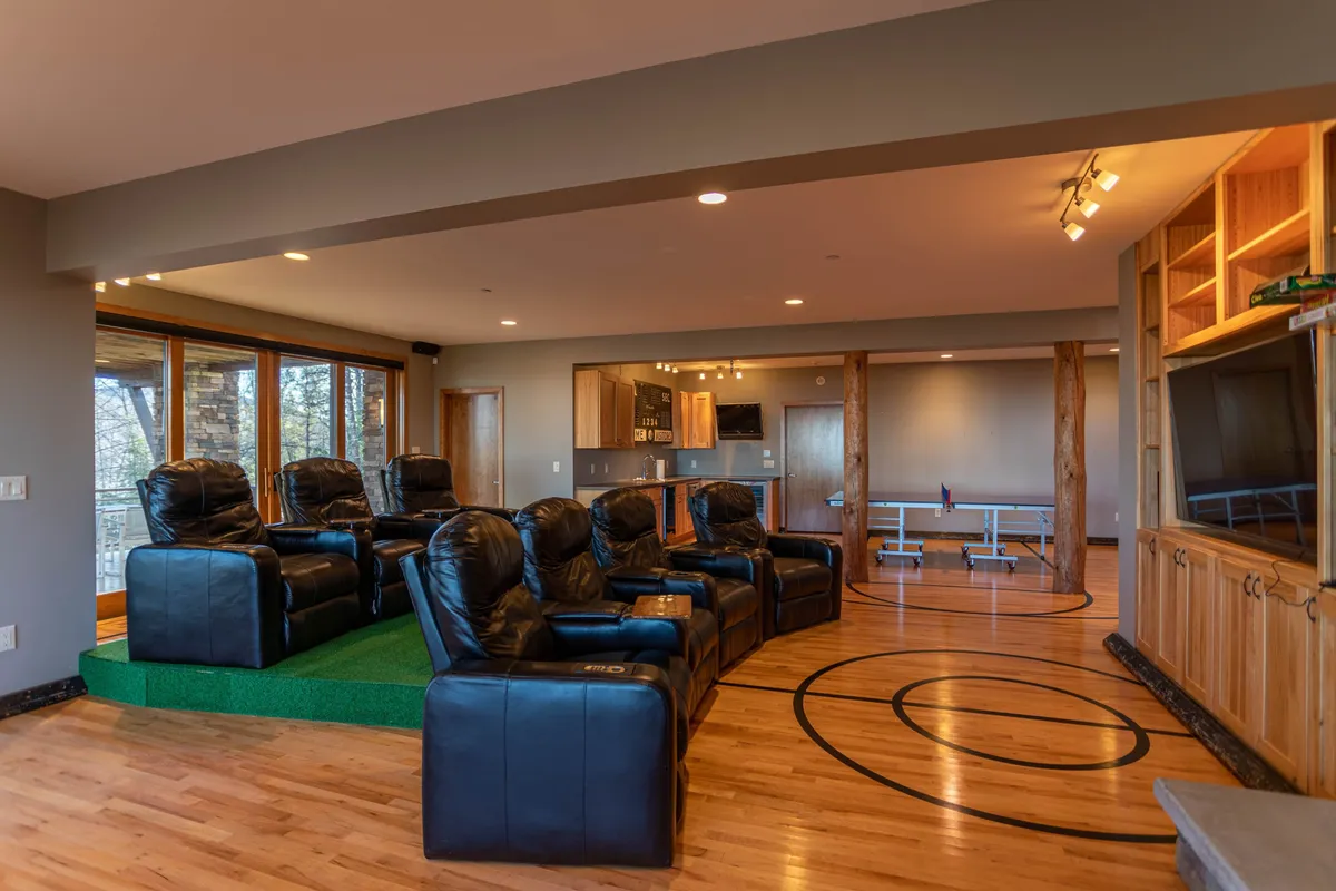 This image showcases a spacious entertainment area with theater-style seating, a large television, wooden accents, and an open kitchen area. The overall ambiance is cozy and inviting, perfect for movie nights or family gatherings.