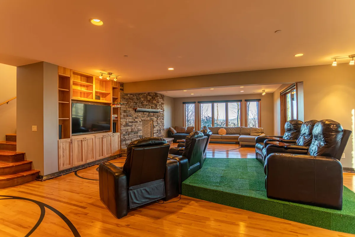 A plush interior with leather recliners facing a stone fireplace, large windows offering scenic views, and custom cabinetry. The setting is perfect for watching movies, social gatherings, or family game nights.