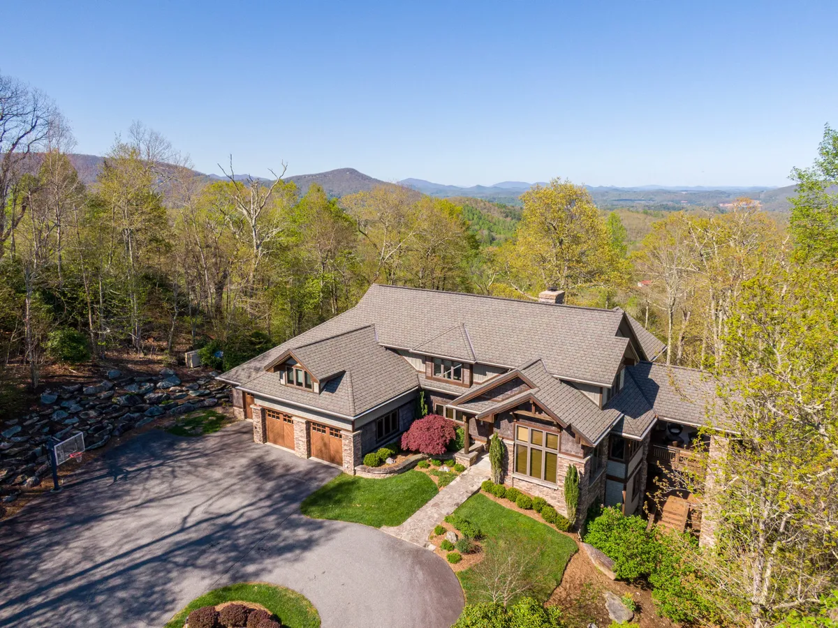 This exterior image showcases a spacious home set against a lush green landscape with a dramatic mountain backdrop and a well-maintained driveway. The house is surrounded by vibrant foliage and natural beauty, highlighting the property's location in the heart of the High Country.