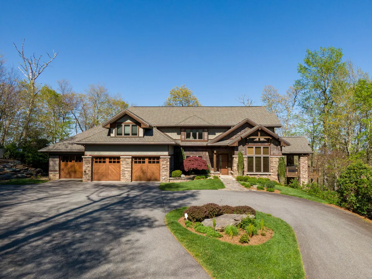 This image showcases the stately house facade, with large windows, beautiful stonework, and a landscaped garden. The driveway leads up to the home, which is set in a serene natural environment, hinting at the grandeur and tranquility within. The space is perfect for gatherings, relaxing mornings, and enjoying the mountain surroundings.