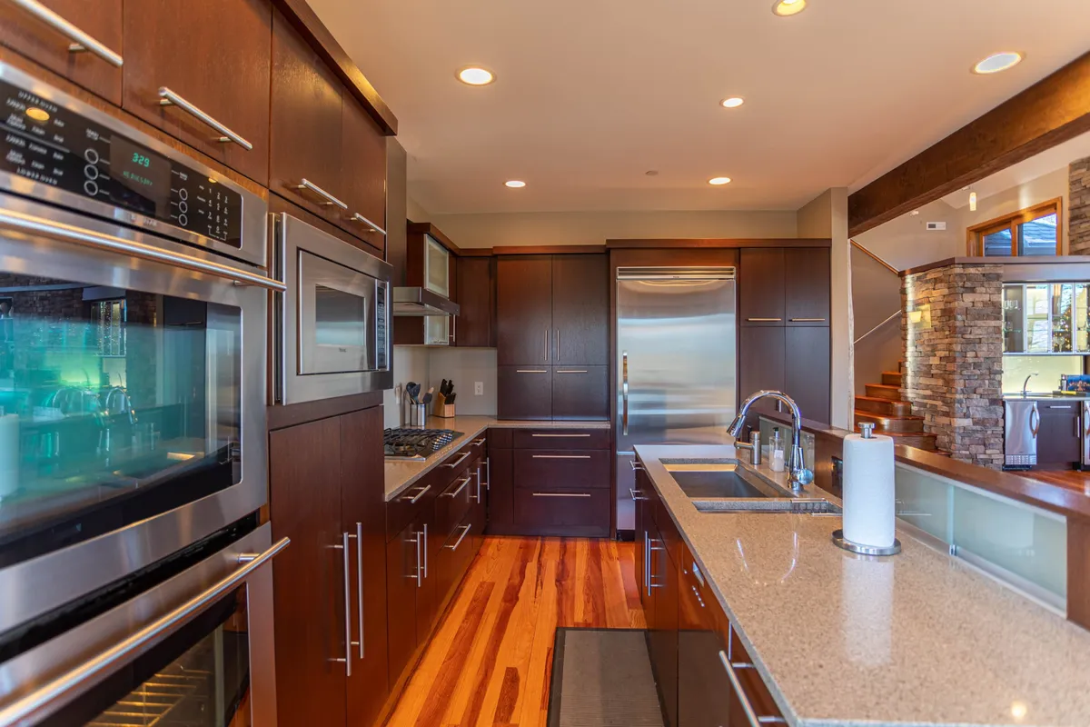A bright, modern kitchen with premium Viking stainless steel appliances, granite countertops, wooden cabinetry, and a large island with a sink. The open layout provides ample space for multiple cooks to gather and prepare meals together.