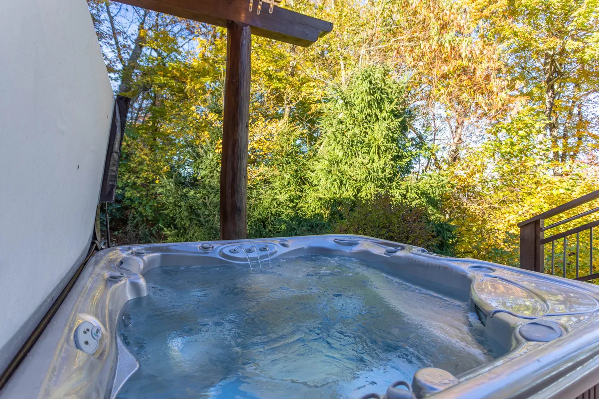 This image highlights a relaxing hot tub area set outdoors amidst lush foliage and a wooden structure. The scene is calm and inviting, suggesting both social opportunities and tranquil, nature-immersed relaxation.